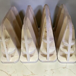 May include: Four unfinished wooden display stands. Each stand has a triangular shape with multiple shelves. The stands are made of light-colored wood and are arranged in a row, perfect for showcasing items.