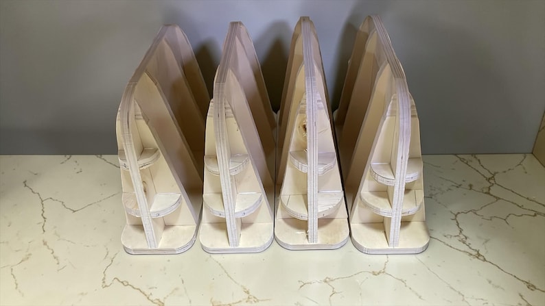 May include: Four unfinished wooden display stands. Each stand has a triangular shape with multiple shelves. The stands are made of light-colored wood and are arranged in a row, perfect for showcasing items.