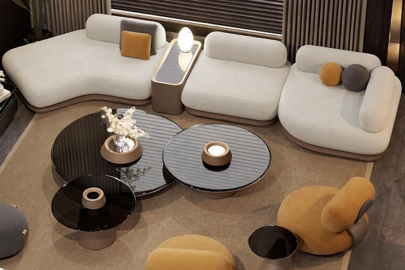May include: An overhead view of a modern living room with white sofas, black glass coffee tables, and a mustard-colored armchair. The sofas have rounded edges and are arranged in a curved layout. Decorative pillows in gray and mustard add color.