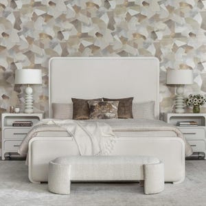 May include: A contemporary bedroom suite featuring a white bed frame, headboard, and a matching bench. Two white bedside tables with lamps and drawers are on either side of the bed. Decorative cushions and a throw blanket add texture. The wallpaper has an abstract design.