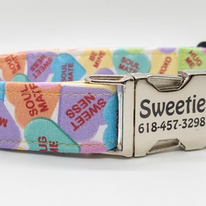May include: A colorful dog collar with a repeating pattern of pastel-colored conversation hearts. The hearts display phrases like "Be Mine" and "Soul Mate." The collar has a silver metal buckle with the name "Sweetie" and a phone number.