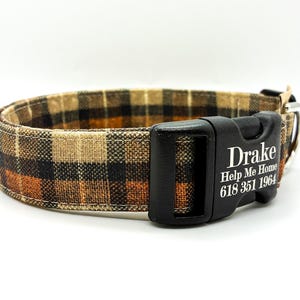 May include: A plaid dog collar in shades of brown, black, and orange. The black plastic buckle features the name "Drake", the phrase "Help Me Home", and a phone number.