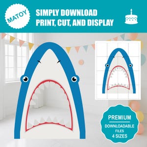 Op de afbeelding: Een grote, blauw en witte haai-vormige foto booth prop met een wijd open mond, rode accenten en cartoon ogen. De tekst "SIMPLY DOWNLOAD PRINT, CUT, AND DISPLAY" staat boven de haai. Een kleinere versie van de haai is rechts afgebeeld.