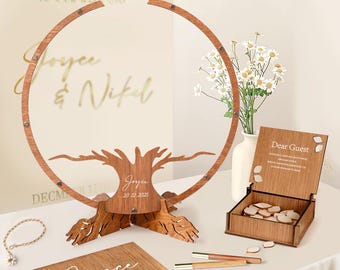May include: A wooden wedding guest book set. The set includes a tree-shaped guest book with a circular frame, a wooden box with guest tokens, and a wooden guest book. The tree has the names "Joyce & Nikel" and the date "20.12.2025".