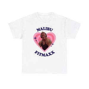May include: White t-shirt featuring a graphic of a man inside a pink heart with the words "MALIBU" above and "FITMAXX" below in navy blue. The man is wearing headphones and a black tank top.