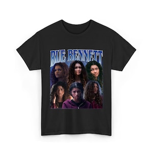 Può includere: T-shirt nero con grafica di Rue Bennett della serie TV Euphoria. Il design include più immagini del personaggio con la scritta "RUE BENNETT" in un font blu in stile vintage. Una maglietta girocollo.