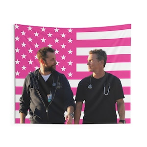 Könnte beinhalten: Ein Wandteppich mit zwei Personen in medizinischer Kleidung vor einer rosa-weißen amerikanischen Flagge. Die Sterne und Streifen der Flagge sind deutlich zu sehen. Die Personen tragen schwarze Hemden und haben Stethoskope um den Hals.