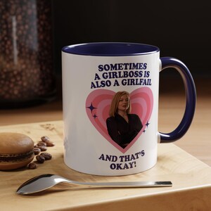 Peut inclure: Mug en céramique blanche avec intérieur et anse bleu marine. Le mug présente le texte "SOMETIMES A GIRLBOSS IS ALSO A GIRLFAIL AND THAT'S OKAY!" ainsi qu'une image d'une femme dans un cœur rose.