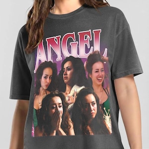 Pode incluir: Camiseta cinza escuro com a palavra "ANGEL" em letras rosa e brancas. A camiseta apresenta uma colagem de imagens de uma mulher com várias expressões faciais. A mulher está usando um top verde em algumas imagens.