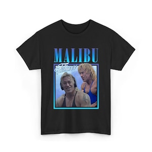 May include: Black t-shirt featuring a retro design with the text "MALIBU Fitness" above a framed image of two men. The image has a blue and purple gradient background. The men are wearing workout attire.