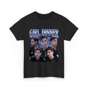 Può includere: T-shirt nera con la scritta "GIRL DINNER" in blu e bianco. La grafica presenta più immagini di una persona in un contesto medico, con un effetto fulmine blu sullo sfondo.