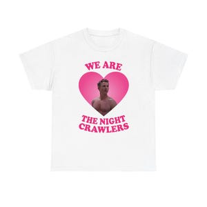 Peut inclure: T-shirt blanc avec un motif de cœur rose. À l'intérieur du cœur, une photo d'un homme. Le texte "WE ARE" est au-dessus du cœur, et "THE NIGHT CRAWLERS" est en dessous, en rose.