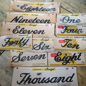 May include: A collection of ten vintage Creative Script letter stickers. The stickers are printed on white paper with black lettering and yellow accents. The letters include: Eighteen, Nineteen, One, Eleven, Four, Forty, Six, Ten, Seven, Eight, and Thousand.