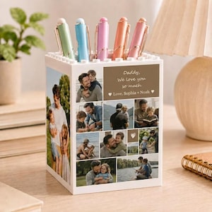 May include: A white pen holder with a collage of family photos and the text "Daddy, We love you so much". The holder contains pens in green, blue, pink, orange, and pink. A thoughtful gift for a father.