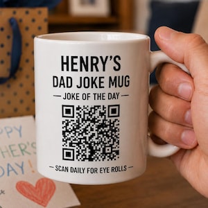 May include: A white ceramic mug featuring black text that reads HENRY'S DAD JOKE MUG, JOKE OF THE DAY, and SCAN DAILY FOR EYE ROLLS. A large black and white QR code is printed in the center of the mug, positioned between the text lines.