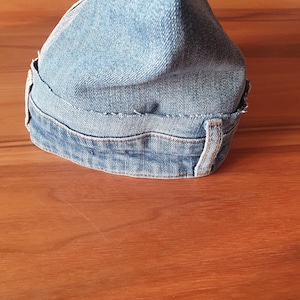 May include: A denim fabric shift knob cover in light blue. The cover is made from recycled denim and features visible stitching and belt loops. The cover is designed to fit over a car's shift knob.