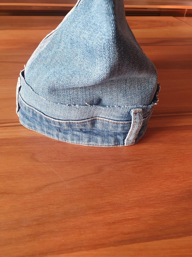 May include: A denim fabric shift knob cover in light blue. The cover is made from recycled denim and features visible stitching and belt loops. The cover is designed to fit over a car's shift knob.
