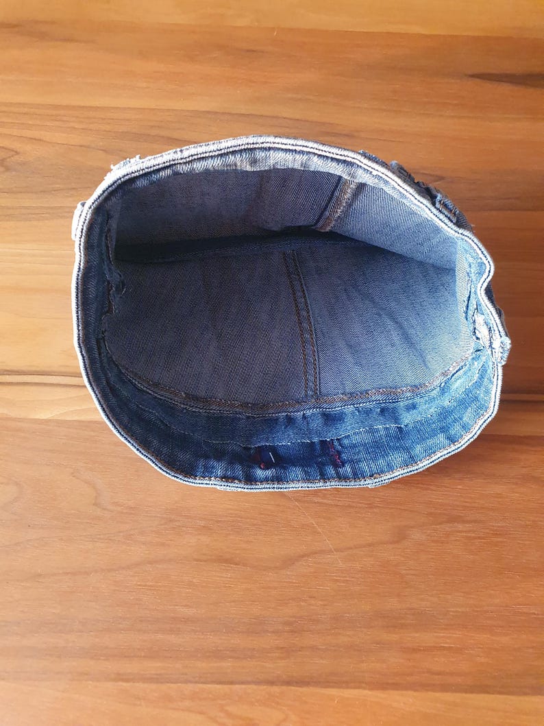 May include: A denim cap, viewed from the inside, showcasing the blue fabric and stitching details. The cap's brim is visible, and the interior reveals the construction and shape of the hat. The cap is set against a wooden surface.