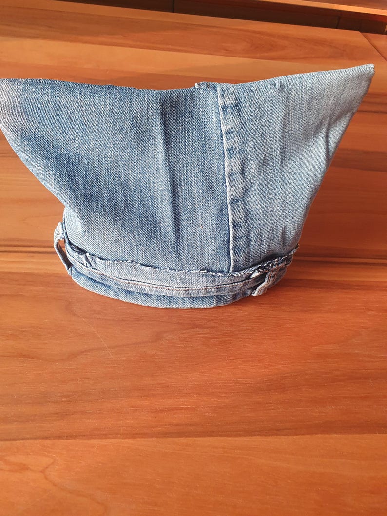 May include: A light blue denim hat with a pointed crown and a curved brim. The hat is made from a light wash denim material and features visible stitching details. The brim is secured with a denim band.