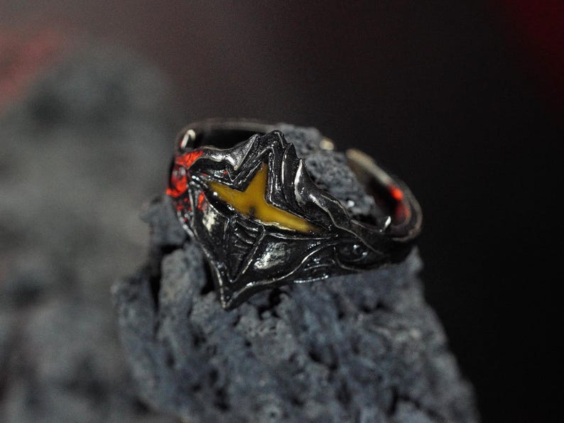 Puede incluir: Un anillo de plata con un dise&ntilde;o negro y amarillo. El anillo est&aacute; colocado sobre un fondo gris oscuro.