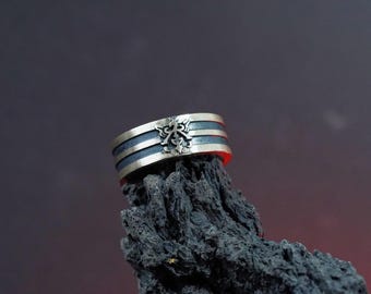 May include: A silver ring with a black inlay and a stylized design. The ring is sitting on a piece of dark gray rock.