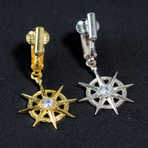 Op de afbeelding: Een paar gouden en zilveren stervormige oorbellen met heldere strass steentjes. De oorbellen zijn van het clip-on type.