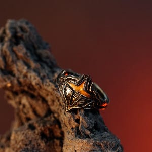 Puede incluir: Un anillo de plata con un dise&ntilde;o detallado que presenta una piedra amarilla en forma de estrella. El anillo est&aacute; apoyado en un trozo de madera desgastada.