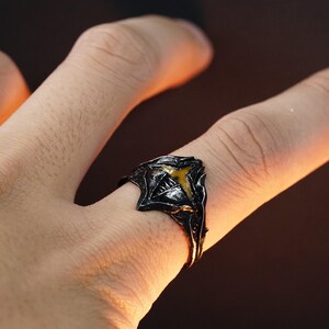 Puede incluir: Un anillo negro con una piedra amarilla en el centro. El anillo est&aacute; dise&ntilde;ado con una forma afilada y angular.