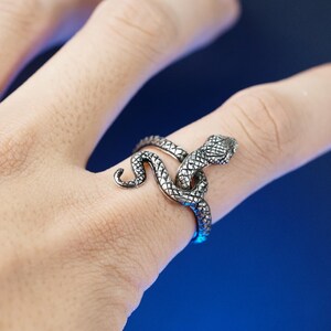 May include: A silver snake ring with a detailed design. The snake is coiled around the finger and the head is facing forward.