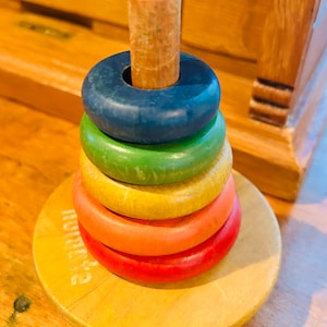 May include: A classic wooden stacking toy with a colorful rainbow of rings. The rings are blue, green, yellow, orange, and red. The toy is on a wooden base.