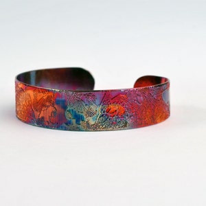 Op de afbeelding: Een koperen armband met een kleurrijk, abstract ontwerp. De armband is gemaakt van metaal en heeft een gladde, gepolijste afwerking.