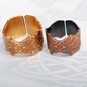 May include: Two decorative metal rings with intricate floral patterns. The ring on the left is gold, and the ring on the right is copper.