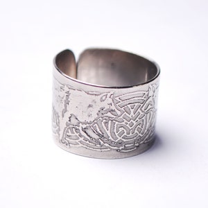 Peut inclure: Une bague en argent avec une large bande ornée d'un motif complexe de nœud celtique. La bague est en métal et a une finition polie.