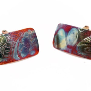 May include: A pair of rectangular cufflinks with a swirling, abstract design in shades of red, blue, green, and gold.