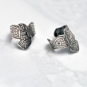 May include: Two silver ear cuffs with intricate geometric designs. The cuffs are open and have a slightly curved shape.