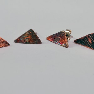 Puede incluir: Un conjunto de cuatro pendientes de triángulo de cobre con diseños intrincados. Los pendientes tienen un poste de plata y un cierre de mariposa.