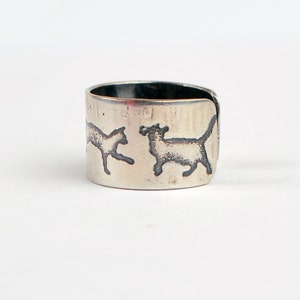 May include: A silver ring with two cats etched into the band. The cats are facing opposite directions and are in a running pose.