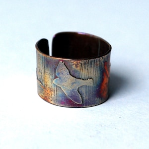 Könnte beinhalten: Ein Kupferring mit einer strukturierten Oberfläche und einem Vogelmotiv. Der Ring hat einen rustikalen, Vintage-Look und ist ein einzigartiges Schmuckstück.