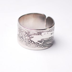 Op de afbeelding: Een zilveren ring met een ingewikkeld ontwerp van een vogel met uitgespreide vleugels. Het ontwerp is in het metaal gegraveerd.