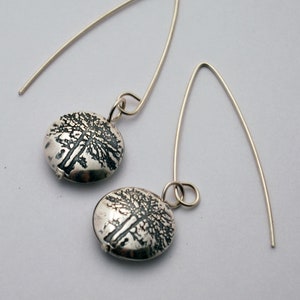 May include: A pair of silver earrings with a round, textured pendant featuring a tree design.