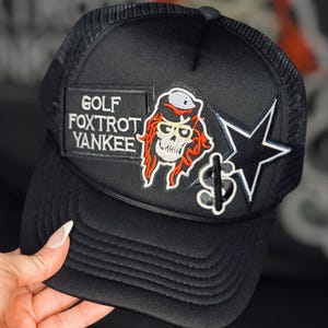 May include: Black trucker hat with a skull and crossbones patch, a star patch, and a patch that says "GOLF FOXTRT YANKEE"