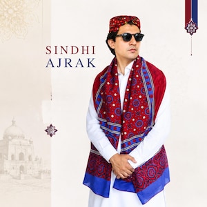 May include: A man wearing a Sindhi Ajrak scarf and cap. The scarf is red with blue and white geometric patterns. The cap has a similar design. The text "SINDHI AJRAK" is displayed in the image.