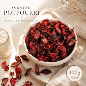 May include: A white bowl filled with red and brown potpourri, with the text "SCENTED POTPOURRI NATURAL BOTANICAL BLEND". A small, round label indicates a weight of 100g. The potpourri is scattered on a light-colored surface.