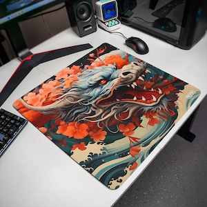 Peut inclure: Un tapis de bureau carré présentant une illustration détaillée d'une tête de dragon aux dents acérées et aux yeux rouges, entourée de motifs floraux orange vifs et de vagues bleues stylisées. Le design intègre des lignes fluides.