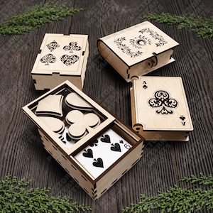 Può includere: Quattro scatole di legno con disegni di carte da gioco. Una scatola è aperta, rivelando le carte da gioco. Le scatole presentano disegni tagliati al laser di cuori, fiori, picche e quadri. Una scatola è a forma di libro con decorazioni floreali.