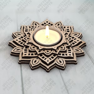 May include: A wooden candle holder with a mandala design. The candle holder is brown with a light-colored interior and holds a lit candle. The design is intricate and geometric, with a floral pattern.