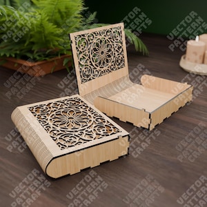 May include: A wooden box with a decorative, intricate laser-cut design. The box is open, revealing the interior. The box is made of light brown wood and has a hinged lid.
