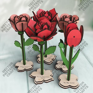May include: Wooden laser-cut flowers in red and pink hues, with green stems and leaves. The flowers are mounted on wooden bases with text that reads "Happy Valentine's Day Anna!", "To my Valentine, Kate!", and "To My Love".