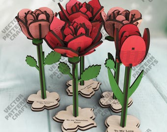 Op de afbeelding: Houten bloemen, lasergesneden in rood en roze tinten, met groene stelen en bladeren. De bloemen zijn gemonteerd op houten voetstukken met de tekst "Happy Valentine's Day Anna!", "To my Valentine, Kate!" en "To My Love".