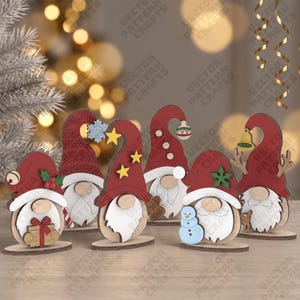 May include: A set of six wooden gnome ornaments featuring red hats and white beards. Each gnome displays unique holiday accents including a gift, a snowflake, yellow stars, a gingerbread man, a blue snowman, and reindeer antlers.